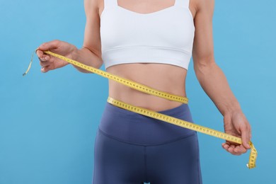 Photo of Slim woman measuring waist with tape on light blue background, closeup. Weight loss