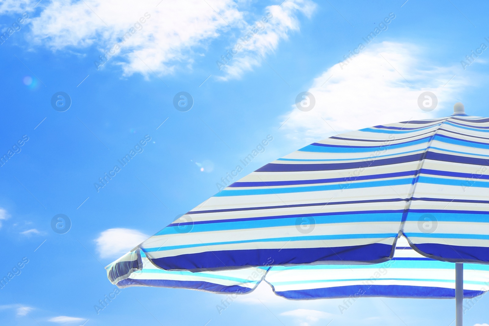 Image of Open big striped beach umbrella and beautiful blue sky with white clouds on background