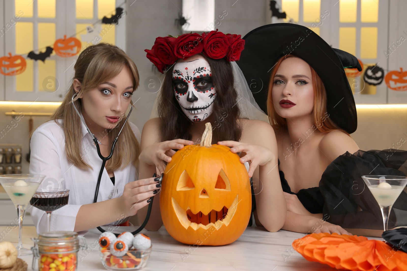 Photo of Group of women in scary costumes with cocktails and carved pumpkin celebrating Halloween indoors