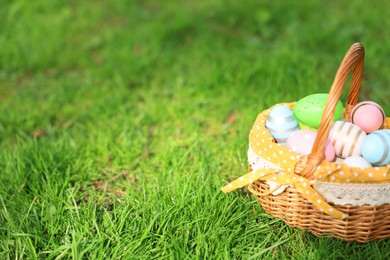 Photo of Easter celebration. Painted eggs in wicker basket on green grass, space for text