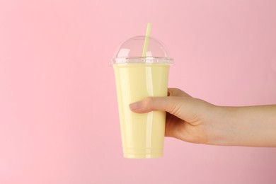 Woman holding plastic cup of tasty smoothie on pink background, closeup