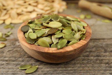 Photo of Bowl with peeled pumpkin seeds on wooden table, closeup