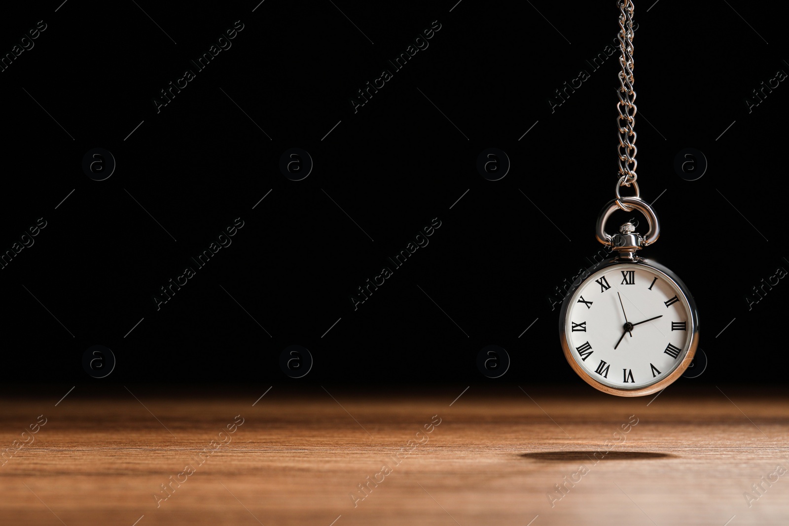 Photo of Beautiful vintage pocket watch with silver chain on black background above wooden table, space for text. Hypnosis session