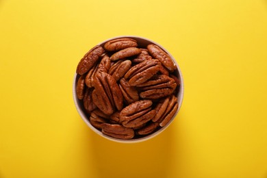 Photo of Tasty pecan nuts in bowl on yellow background, top view