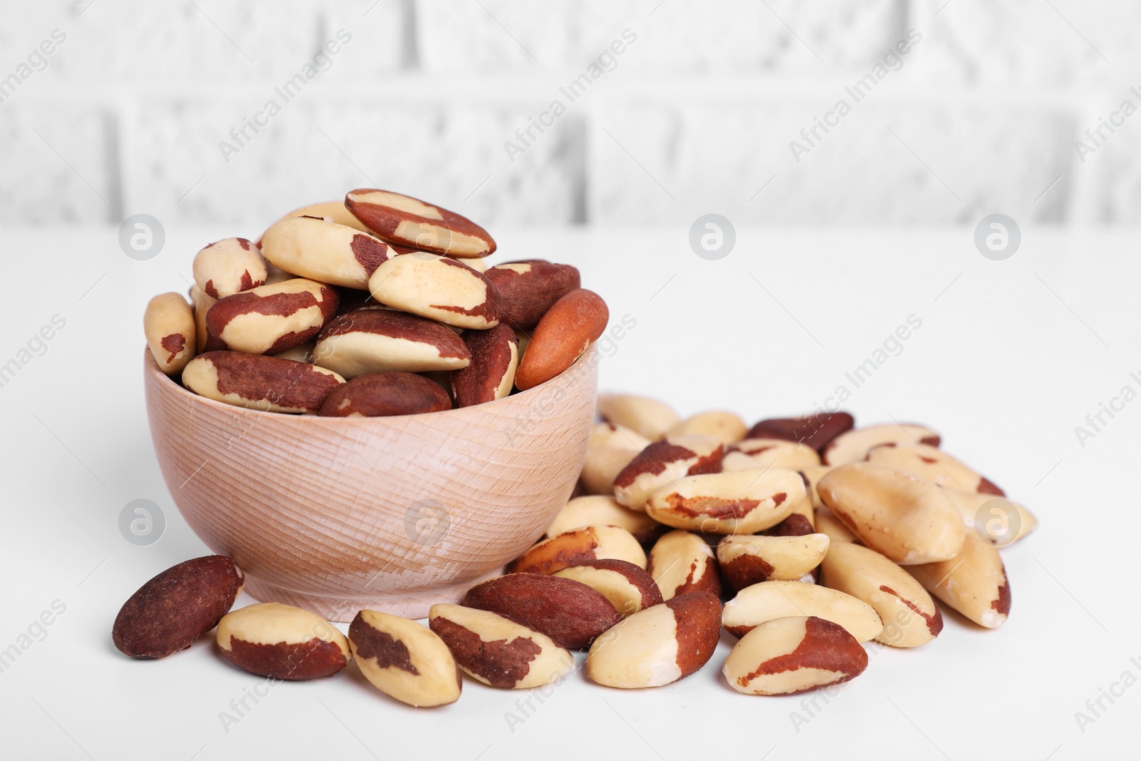 Photo of Tasty Brazil nuts on white table against brick wall
