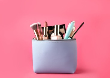 Cosmetic bag with makeup products and accessories on pink background