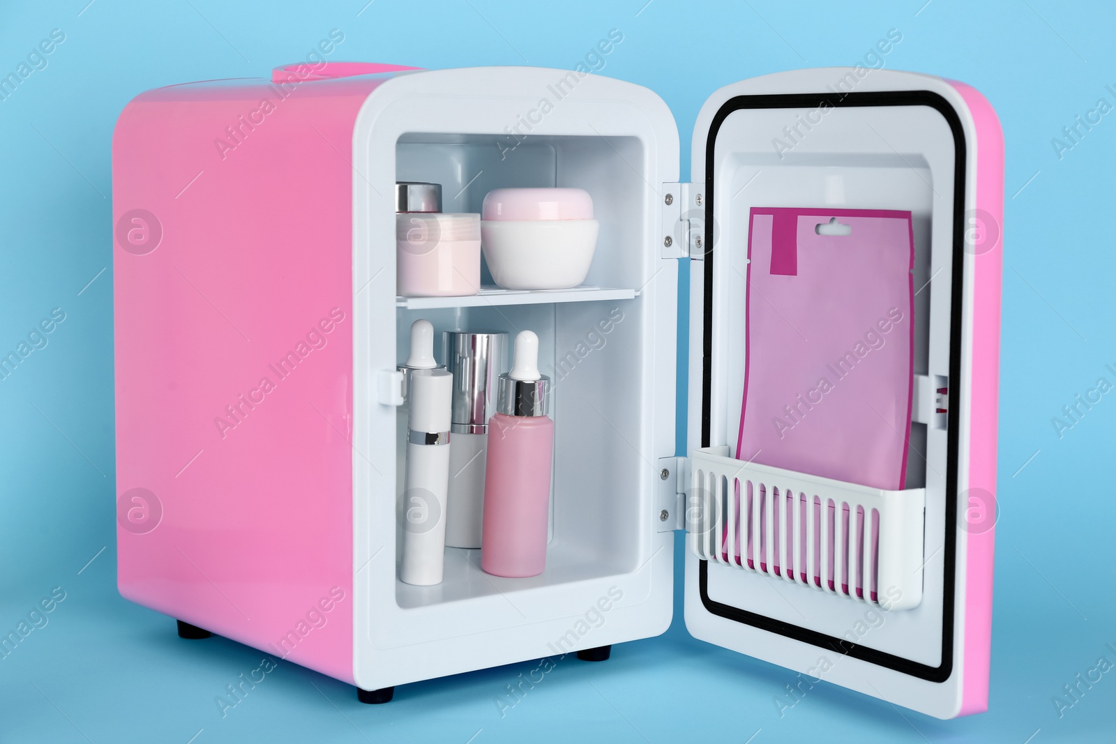 Photo of Pink cosmetics refrigerator with skin care products on light blue background