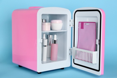 Pink cosmetics refrigerator with skin care products on light blue background