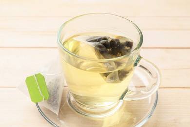 Tea bag in glass cup on light wooden table, closeup