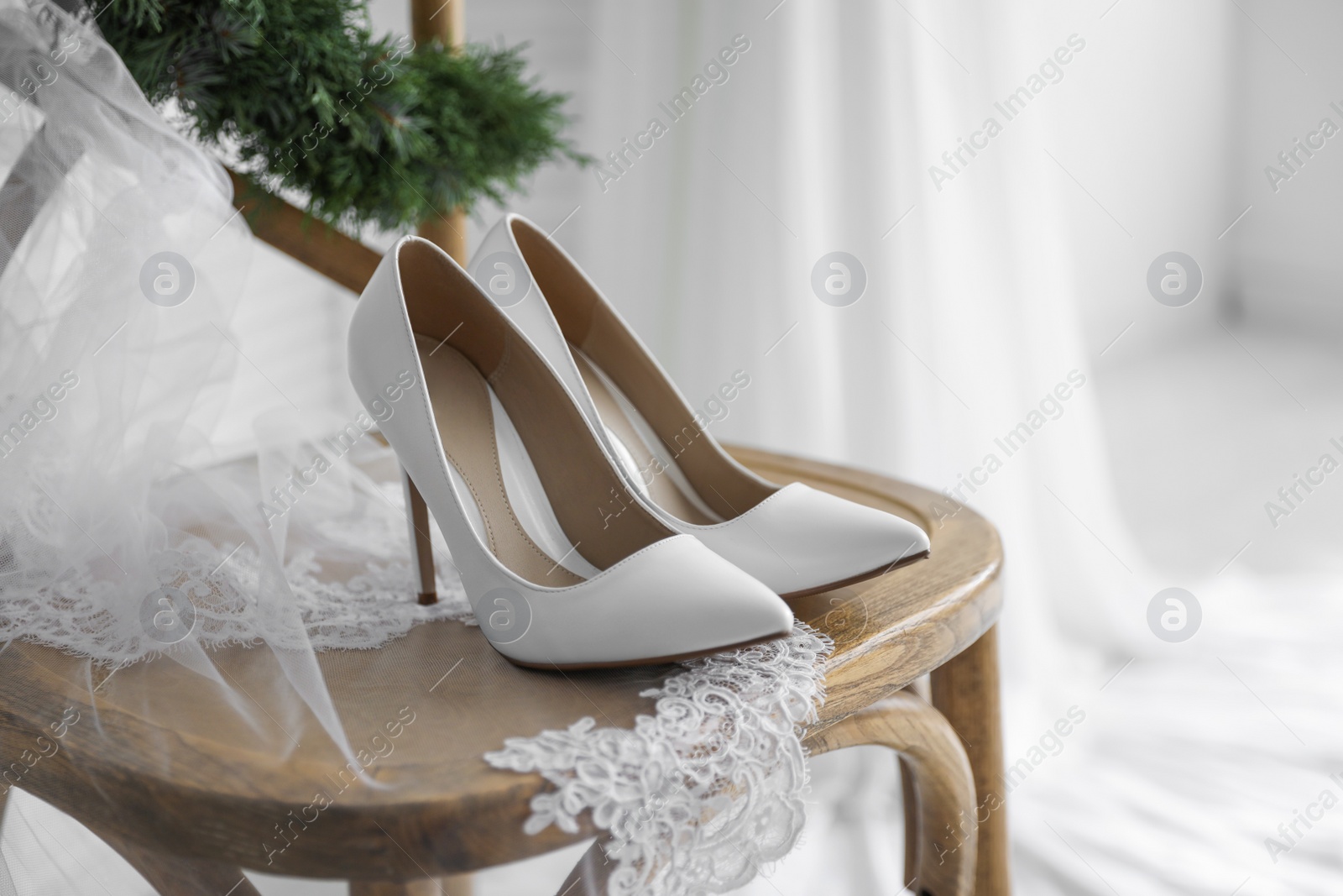 Photo of Pair of white high heel shoes, veil and wreath on wooden chair indoors. Dressing for wedding