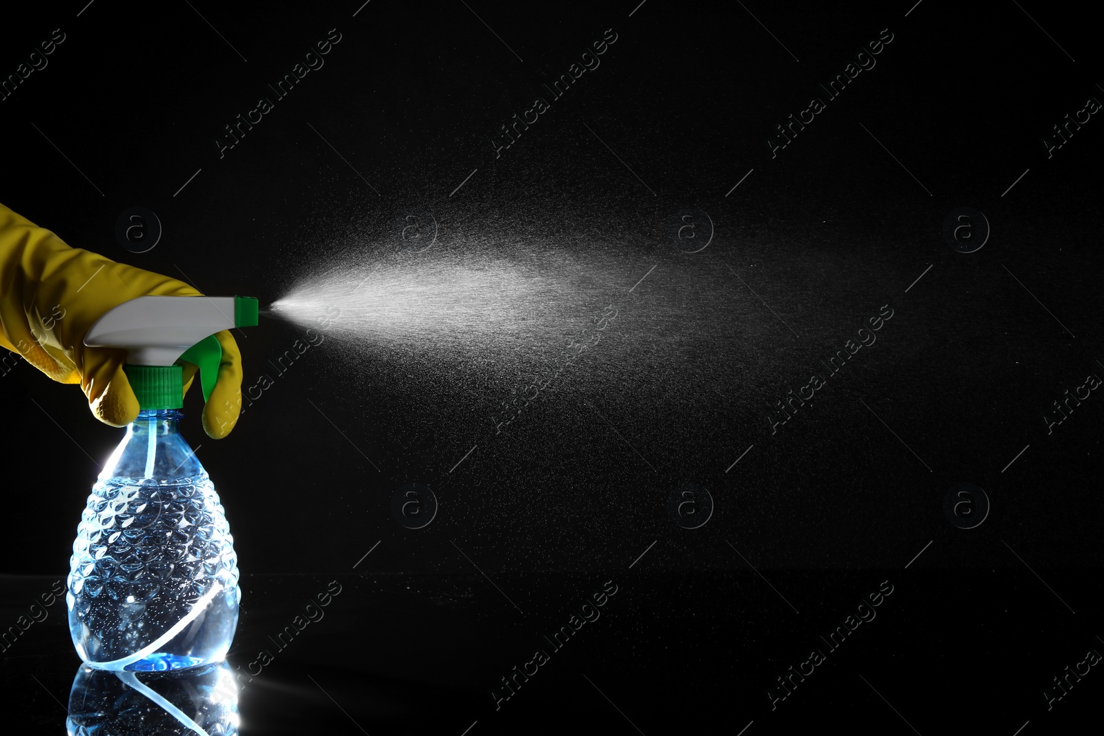 Photo of Woman spraying liquid from bottle on black background, closeup