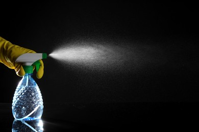 Photo of Woman spraying liquid from bottle on black background, closeup