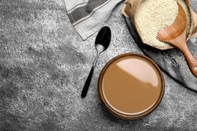 Tasty sesame paste and seeds on grey table, flat lay. Space for text