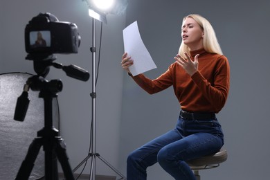 Photo of Casting call. Emotional woman with script sitting on chair and performing in front of camera in studio