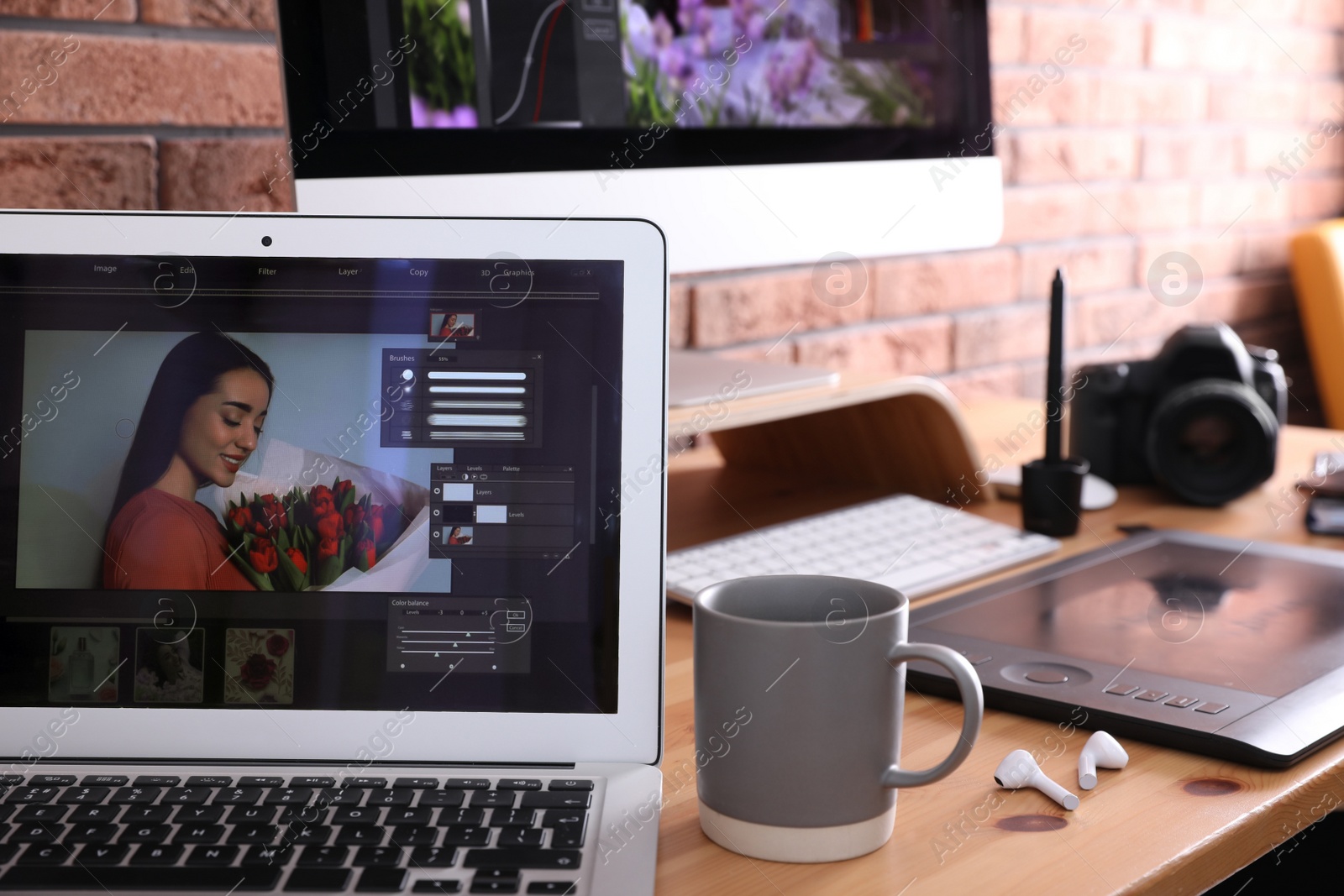 Photo of Modern retoucher's workplace with different digital devices on wooden table near red brick wall