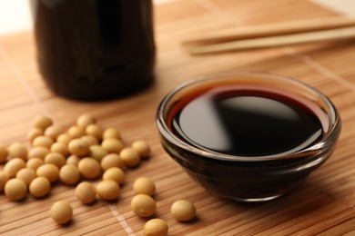 Photo of Soy sauce in bowl and soybeans on bamboo mat, closeup