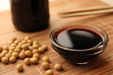 Soy sauce in bowl and soybeans on bamboo mat, closeup