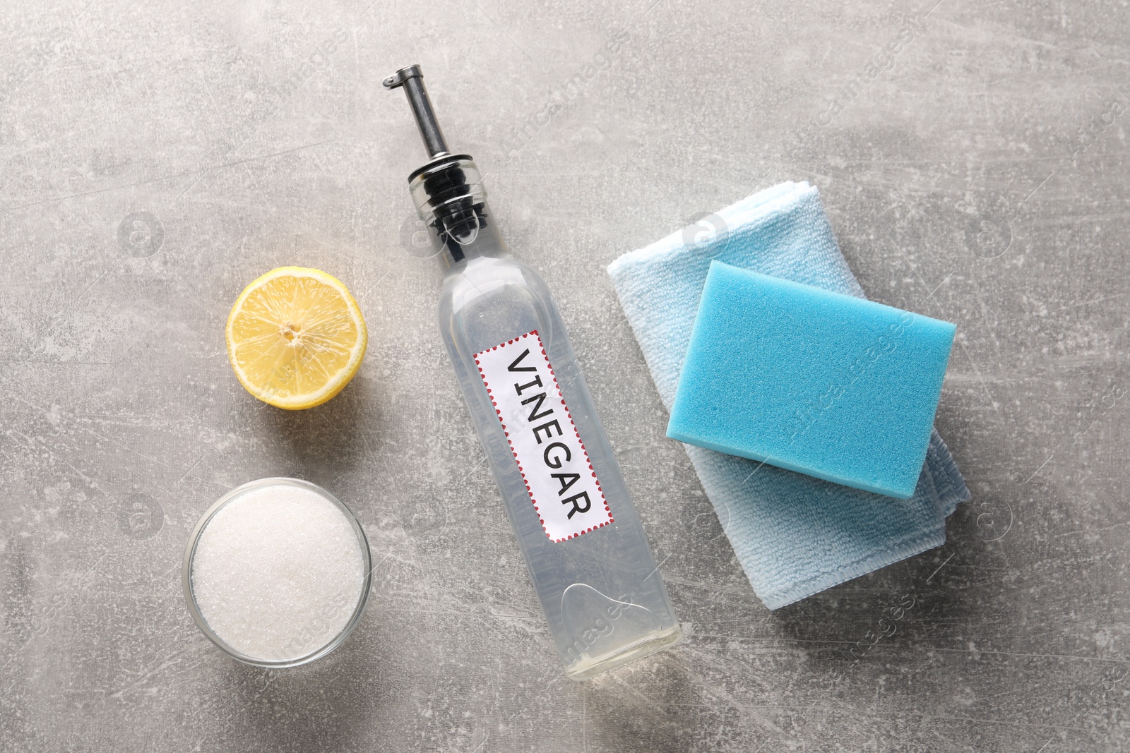 Photo of Natural cleaning products. Vinegar in bottle, baking soda, lemon, rag and sponge on grey textured table, flat lay