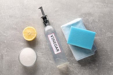 Natural cleaning products. Vinegar in bottle, baking soda, lemon, rag and sponge on grey textured table, flat lay