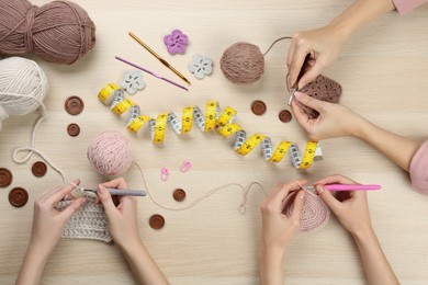 Photo of Women crocheting with threads at wooden table, top view