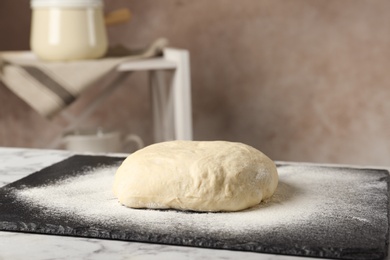 Photo of Board with flour and bread dough on table indoors. Space for text