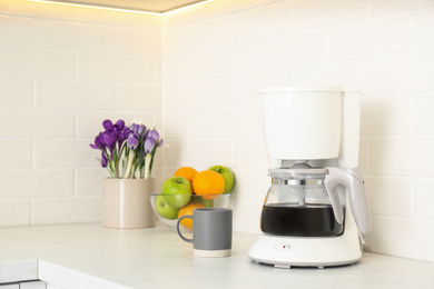 Coffeemaker, cup, fruits and flowers on counter in kitchen