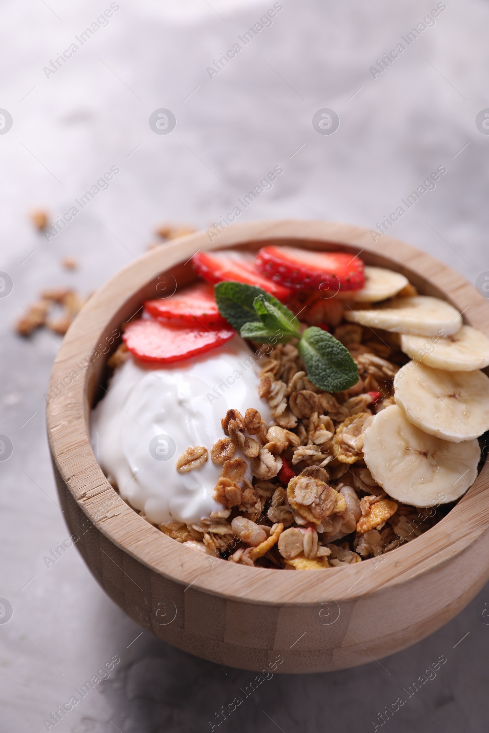 Photo of Tasty granola with yogurt, banana and strawberry in bowl on gray textured table, closeup