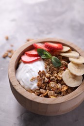 Photo of Tasty granola with yogurt, banana and strawberry in bowl on gray textured table, closeup