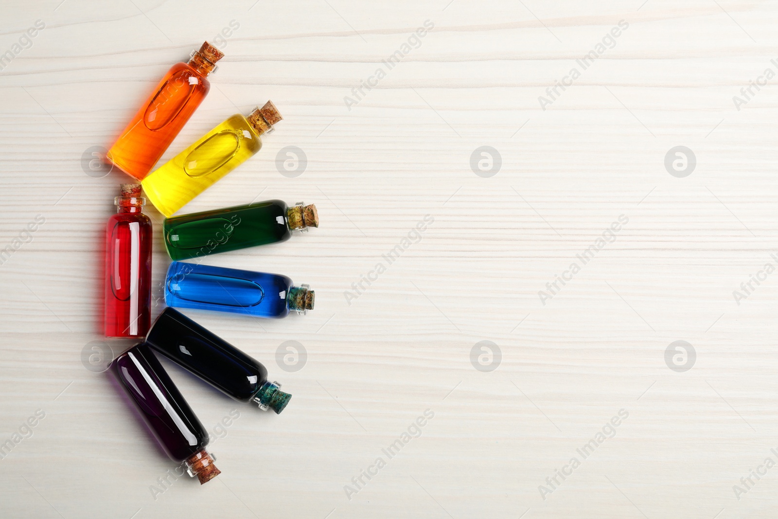 Photo of Glass bottles with different food coloring on white wooden table, flat lay. Space for text