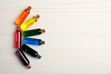 Glass bottles with different food coloring on white wooden table, flat lay. Space for text