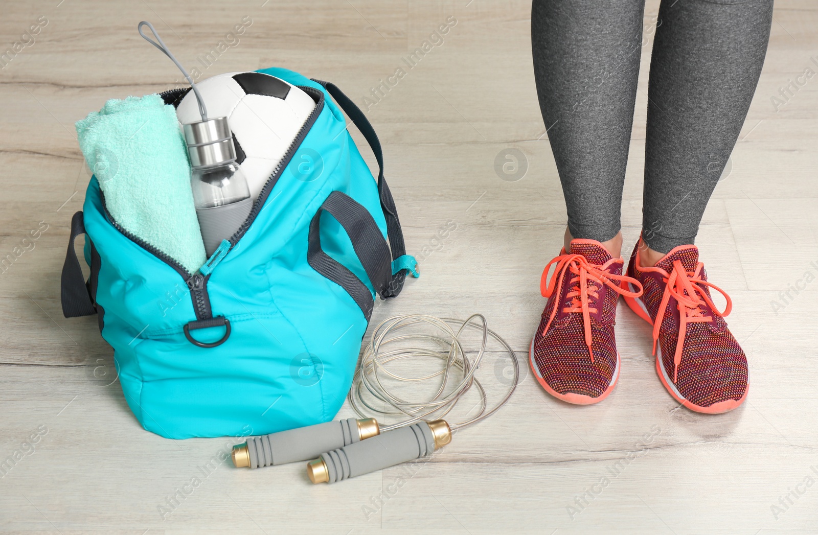 Photo of Young woman in sportswear and bag with gym equipment indoors