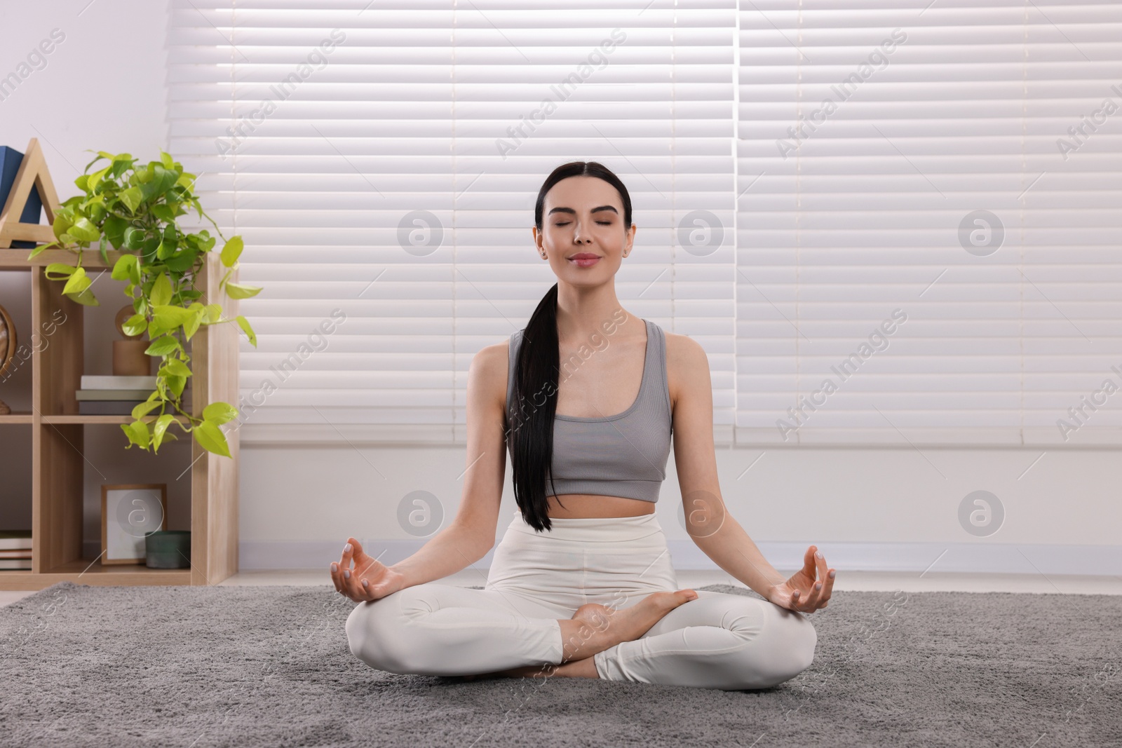 Photo of Woman in sportswear meditating at home. Harmony and zen