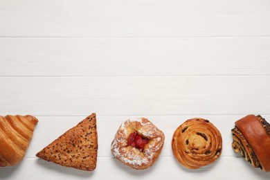 Photo of Different tasty freshly baked pastries on white wooden table, flat lay. Space for text