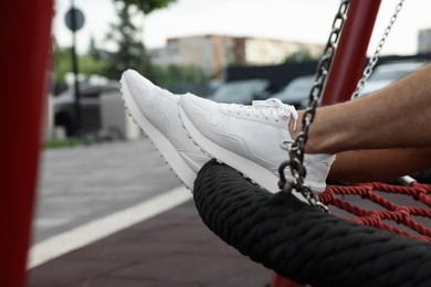 Photo of Man in stylish sneakers sitting on swing outdoors, closeup