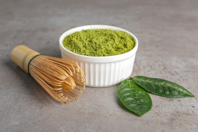 Photo of Green matcha powder, bamboo whisk and leaves on light grey table, closeup