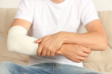 Photo of Man with arm wrapped in medical bandage on sofa, closeup