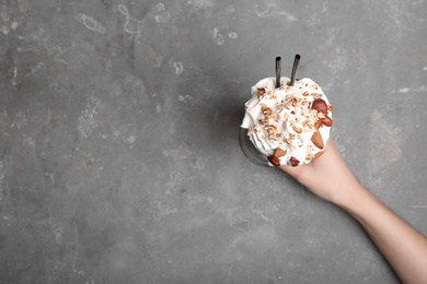Photo of Woman holding glass of delicious milk shake with whipped cream at table, top view