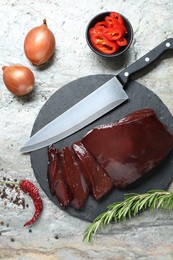 Photo of Cut raw beef liver with rosemary, chili pepper, onions and knife on grey table, flat lay