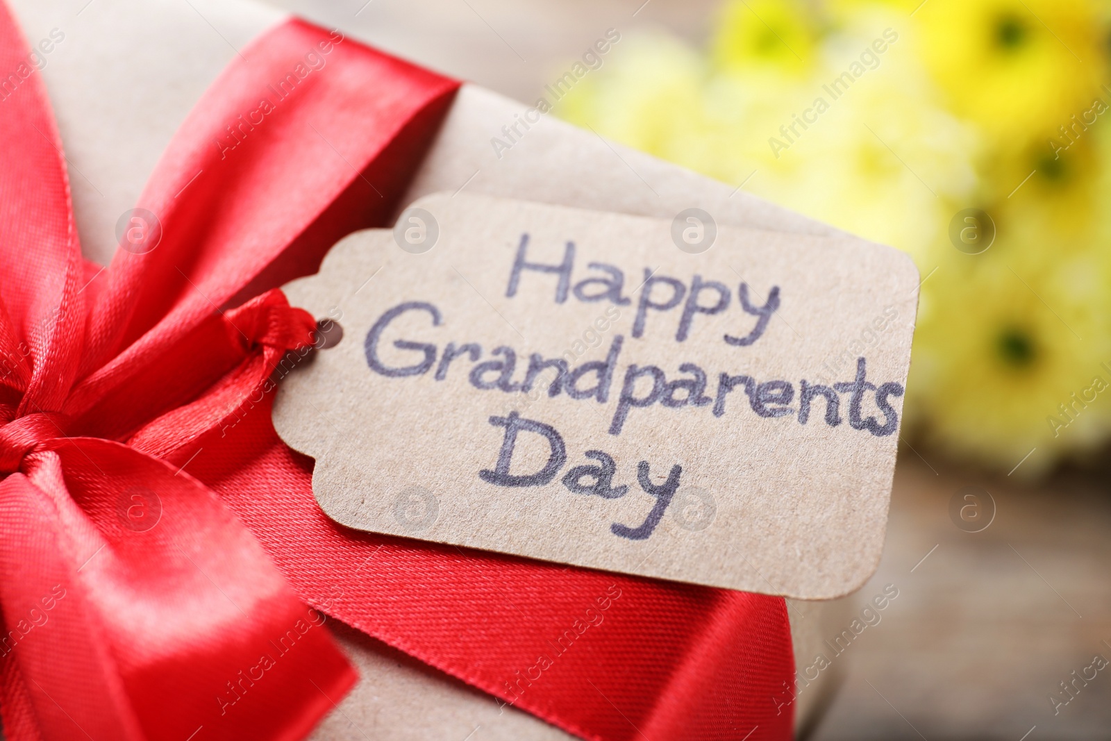 Photo of Beautiful gift box and tag with phrase Happy Grandparents Day on table, closeup