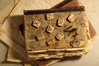Photo of Wooden runes and old books on beige table, top view
