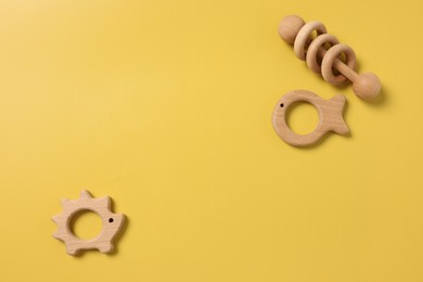 Photo of Baby accessories. Wooden rattle and teethers on yellow background, flat lay. Space for text