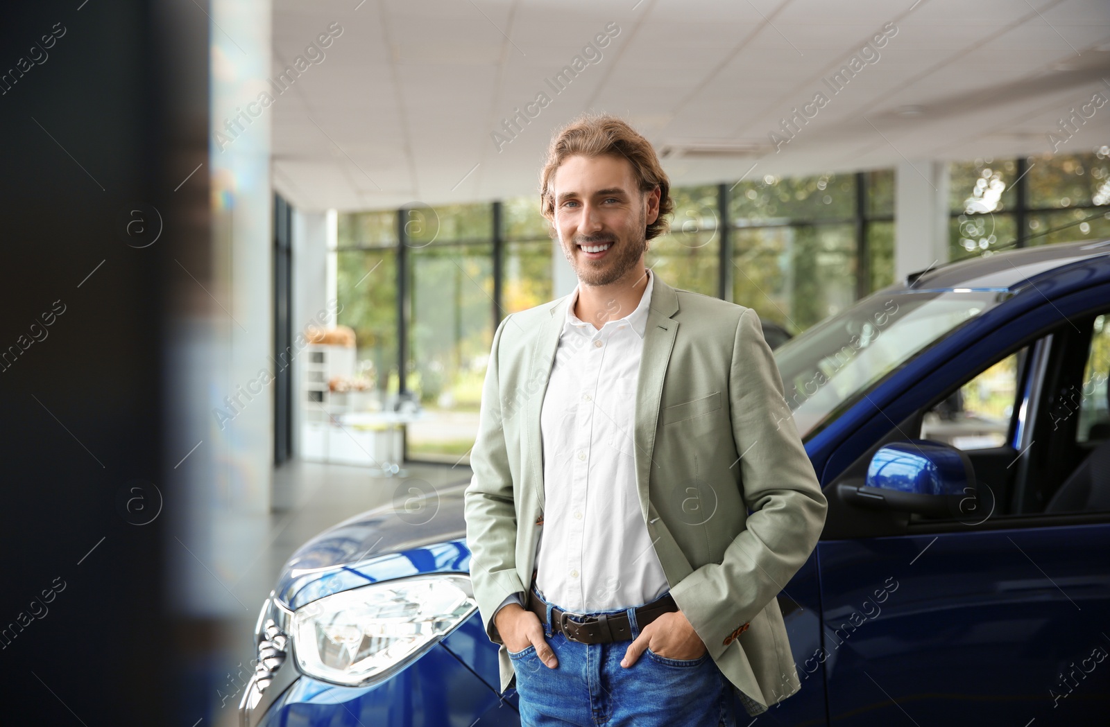 Photo of Young man near new car in modern auto dealership