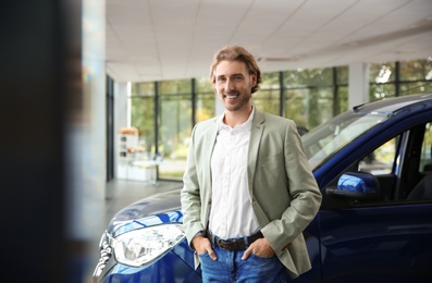 Young man near new car in modern auto dealership