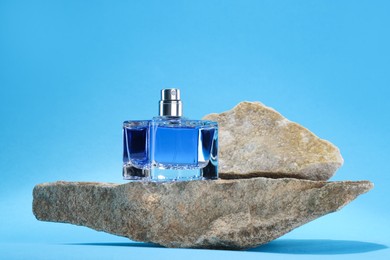 Stylish presentation of luxury men`s perfume on stones against light blue background