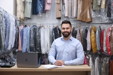 Photo of Dry-cleaning service. Happy worker taking notes at counter indoors