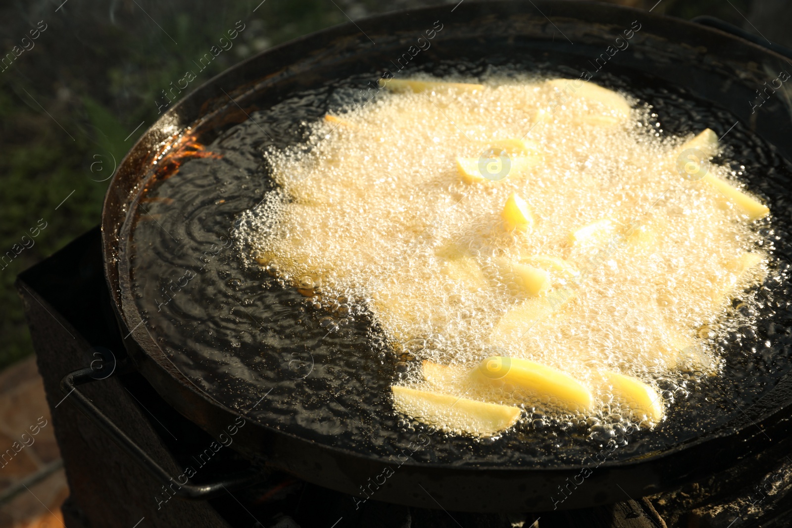 Photo of Cooking delicious potato wedges on frying pan outdoors