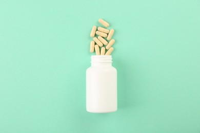 Photo of Bottle and vitamin capsules on turquoise background, top view