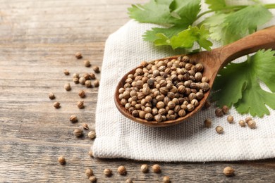 Spoon with dried coriander seeds and green leaves on wooden table, closeup