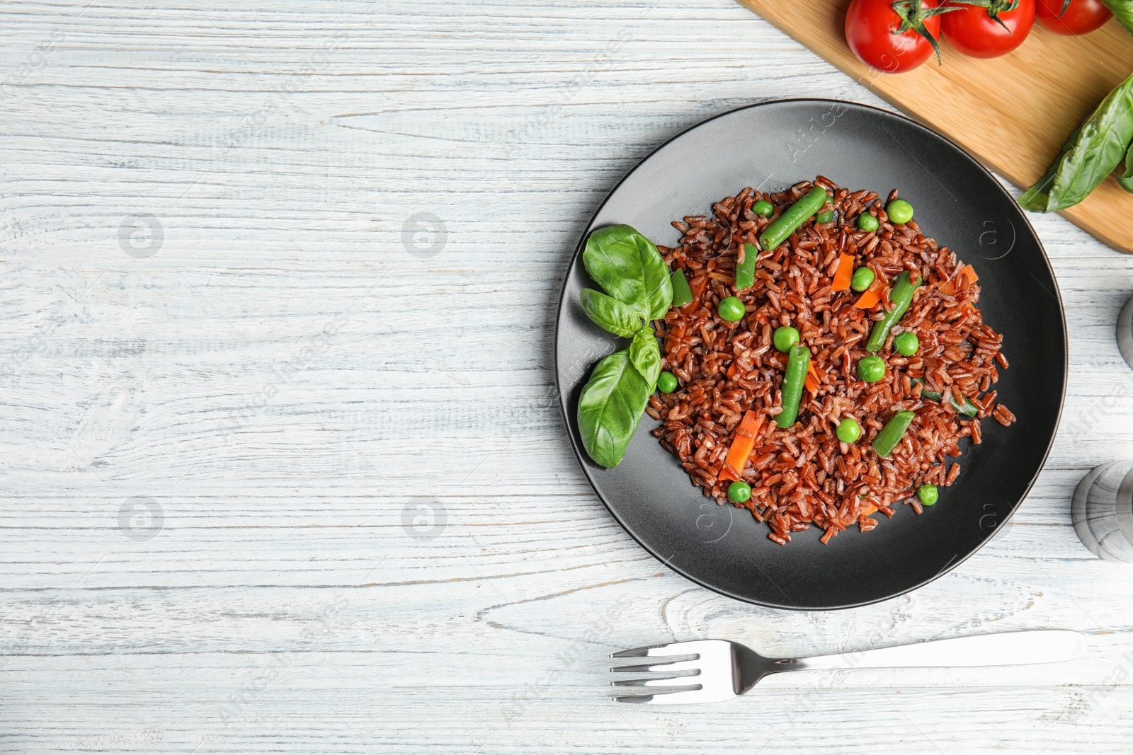 Photo of Plate of brown rice with vegetables on white wooden table, flat lay. Space for text