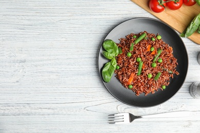 Photo of Plate of brown rice with vegetables on white wooden table, flat lay. Space for text